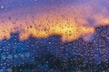 Bright fiery sunset through raindrops on window with bokeh lights. Abstract background. Water drop on the glass against the