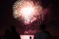 Bright fireworks blast one the beach with silhouetted onlookers