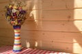 Bright flowers in colorful vase against wooden panel wall on red and white checked tablecloth. Royalty Free Stock Photo