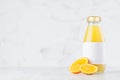 Bright fresh orange juice in glass bottle with blank label template decorated fruit slices in soft light white interior on wood.