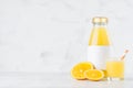 Bright fresh orange juice in glass bottle with blank label template with wine glass decorated straw, fruit slices in soft light.