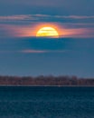 Bright full moon glowing in a hazy night sky popping out from behind clouds on the horizon. Royalty Free Stock Photo