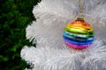 Bright glass rainbow colored Christmas ball, bauble hanging on a white artificial christmas tree. On background of green christmas