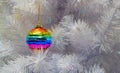 Bright glass rainbow colored Christmas ball, bauble hanging on a white artificial christmas tree. The concept of the holiday,