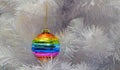 Bright glass rainbow colored Christmas ball, bauble hanging on a white artificial christmas tree. Copy space. The concept of the