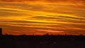 Bright golden sunset sky with winding clouds shining above the silhouettes of trees and houses Royalty Free Stock Photo