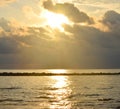 Bright Golden Yellow Sun behind Cloud and Sunbeams, Reflection of Sunlight on Sea Water, Dark Clouds, and Warm Colors in Sky Royalty Free Stock Photo