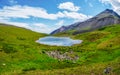 Bright green blue alpine landscape with mountain lake in highland valley in sunlight and big mountain under blue cloudy sky. Royalty Free Stock Photo