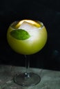 Bright green drink in a goblet glass garnished with basil and lemon