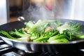 bright green vegetables being stir-fried on an induction cooker