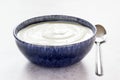 Bright high key image of plain yogurt in blue bowl with spoon aside