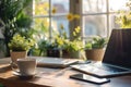 Bright home workspace featuring a laptop, smartphone, coffee cup, and a potted plant, bathed in natural sunlight by the window Royalty Free Stock Photo