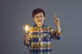 Amazed boy child holding glowing light bulb standing on grey studio background Royalty Free Stock Photo