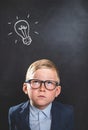 Bright idea. Nerd little kid boy with illustrated bulb above his head against blackboard. Back to school Royalty Free Stock Photo