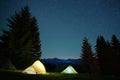 Bright illuminated tourist tents glowing on camping site in dark mountains under night sky with sparkling stars. Active Royalty Free Stock Photo