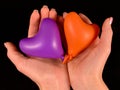 Bright inflatable balloons in the shape of a heart in the hands. Two hearts in female palms, on a black background. Girl holds a