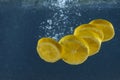 Bright juicy lemon slices with splash and bubbles falling into water isolated over dark blue background, advertisement area Royalty Free Stock Photo