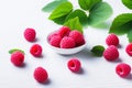 Bright juicy raspberries and green leaves lie in a plate and scattered on a white table. Fresh harvest Royalty Free Stock Photo