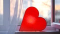 Bright lamp in shape of heart is on window. Concept. Red heart-shaped lamp stands at window and glows to bestow love on