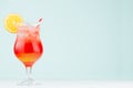 Bright layered red, yellow alcohol cocktail with oranges slice, straw, ice in elegant wineglass on soft light pastel blue.