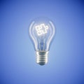 Bright light bulb with a jigsaw puzzle piece on a blue background Royalty Free Stock Photo