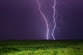 Bright lightnings in dark stormy sky above green field, climate change or weather forecast concept image Royalty Free Stock Photo