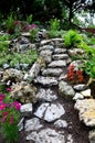 Bright limestone staircase on a rock in the garden. steps of rough stones to a hill with flowers. pink red flowers around the path