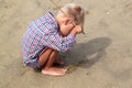 A bright little boy in a plaid shirt thoughtfully holds a stick