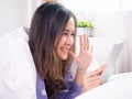 Bright-looking Asian woman is lying on the bed. Use the tablet to talk to video conferencing communicate and talk with people who