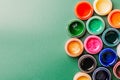 Bright, mother-of-pearl, multicolored open cans of paint on a green background. View from above.