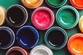 Bright, mother-of-pearl, multicolored open cans of paint on a green background. View from above.