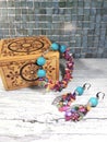 Bright multi-colored bracelet and earrings made of turquoise and mother of pearl with a wooden box on a bright table.