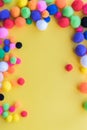 Bright multi-colored pom-poms arranged as a border on a solid yellow background