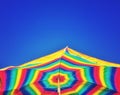 Brightly coloured striped beach umbrella and clear blue sky. Royalty Free Stock Photo