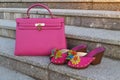 Bright neon pink pair of women`s shoes with handbag on a marble stairs