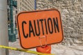 Bright orange Caution sign and yellow tape with stone brick wall background