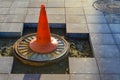 A bright orange cone stands on the sewer drain. marking of dangerous sections on the road, entry for people is prohibited. the