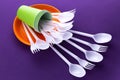 Bright orange and green set of disposable plastic tableware on purple background. Ecology problem. No plastic concept Royalty Free Stock Photo