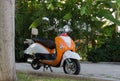 Bright orange moped. A bright orange motorcycle stands by a green bush in the open air. partial focus