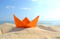 Bright orange paper boat in yellow sand on background of sea waves and blue sky Royalty Free Stock Photo