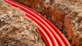 Bright orange protective conduits installed in a dug trench for underground electrical or communication cables amidst rough soil Royalty Free Stock Photo