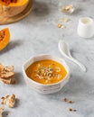 Bright orange pumpkin soup in a white plate on a gray background.