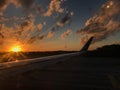 Bright orange sun and the wing of the aircraft during dawn on the runway against the forest silhouette