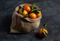 Bright orange tangerines with leaves lie in a burlap sack on a dark background. Christmas fruit. Dark photo