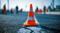 Bright orange traffic cone placed on asphalt road surface with blurred construction workers in the background during daylight for Royalty Free Stock Photo