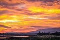 Bright orange and yellow sunset over flat river with a plateau and small trees on the right Royalty Free Stock Photo