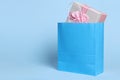 Bright paper shopping bag with gift box on light blue background. Space for text Royalty Free Stock Photo