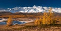 Bright picturesque autumn landscape with mountains covered with snow, forest, yellow larches and beautiful lake with reflections