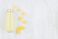 Bright pinapple yellow juice in glass bottle with gold cap, sliced fruit on white wooden board, top view, copy space, template.