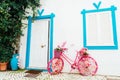 Bright pink bicycle decorated with artificial flowers standing near a white wall with closed window and door of Royalty Free Stock Photo